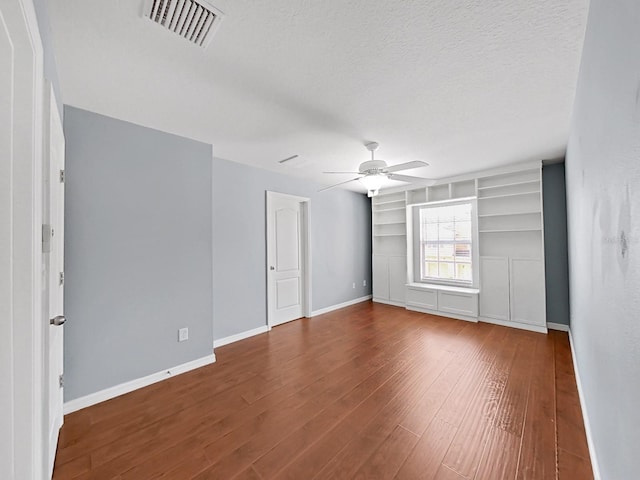 empty room featuring built in shelves, wood-type flooring, a textured ceiling, and ceiling fan