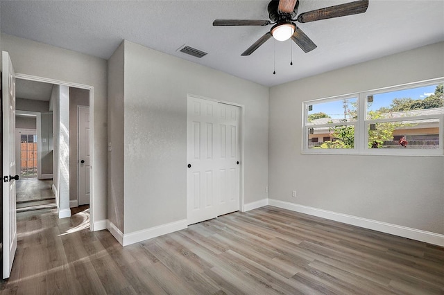 unfurnished bedroom with a closet, a textured ceiling, ceiling fan, and hardwood / wood-style floors