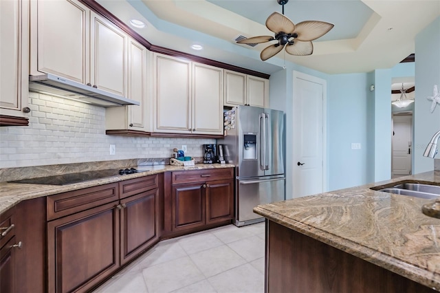 kitchen featuring black electric stovetop, a raised ceiling, a sink, under cabinet range hood, and stainless steel fridge with ice dispenser