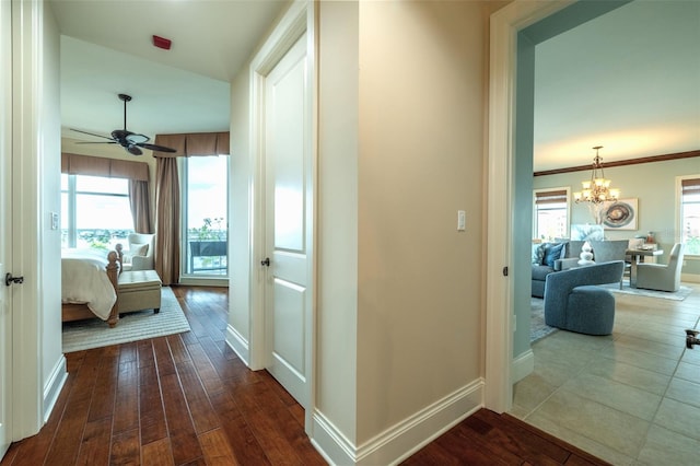 corridor with dark wood-style floors, ornamental molding, baseboards, and an inviting chandelier