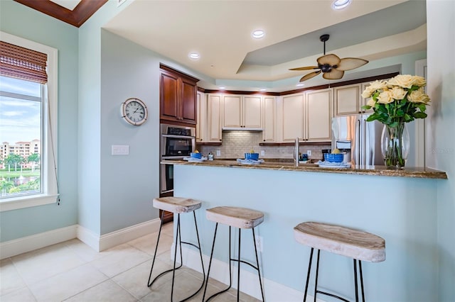 kitchen with a kitchen bar, tasteful backsplash, appliances with stainless steel finishes, a peninsula, and baseboards