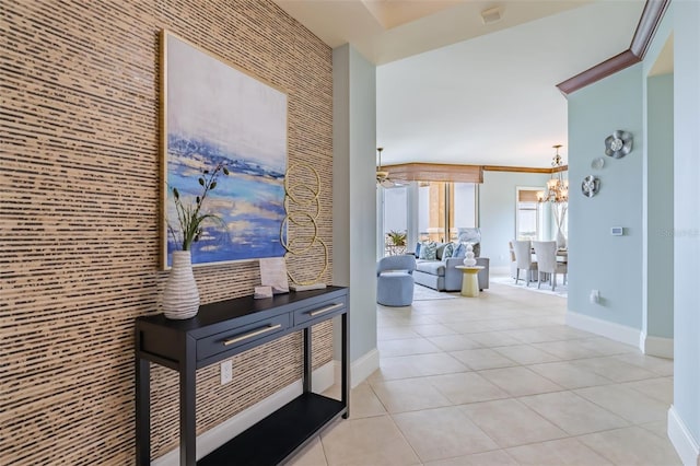 corridor featuring light tile patterned floors, baseboards, an accent wall, and a chandelier