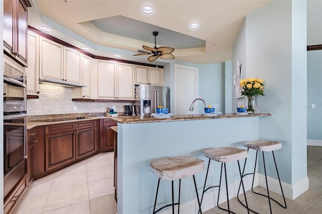 kitchen with black electric cooktop, a breakfast bar, decorative backsplash, a tray ceiling, and stainless steel fridge