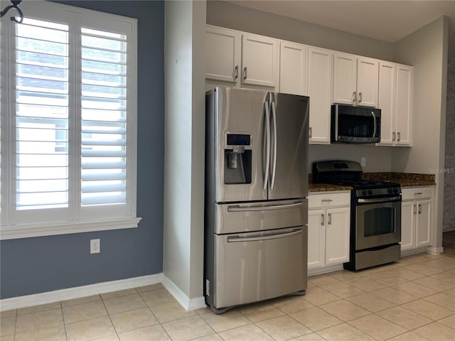 kitchen featuring stainless steel appliances, dark stone counters, white cabinetry, and light tile patterned flooring