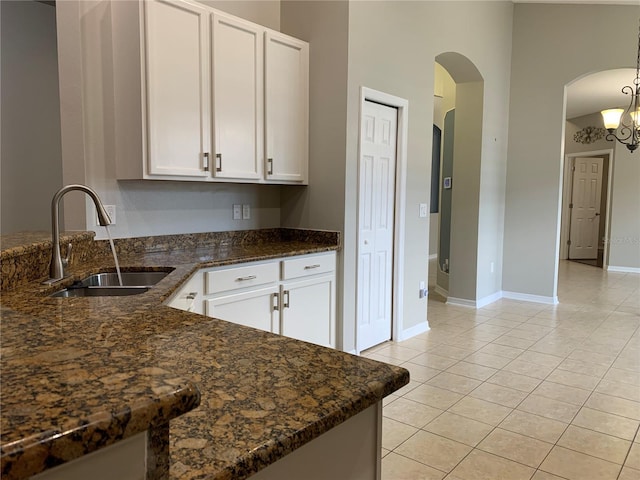 kitchen featuring dark stone counters, light tile patterned floors, sink, an inviting chandelier, and white cabinets