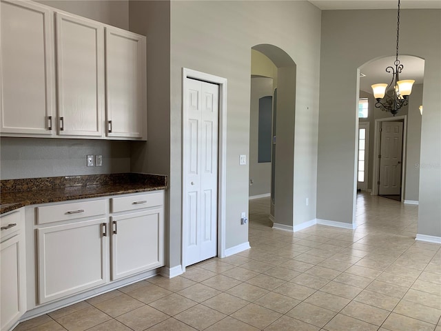 kitchen featuring an inviting chandelier, decorative light fixtures, dark stone countertops, white cabinets, and light tile patterned flooring