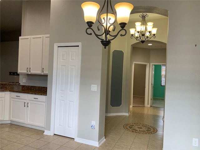 kitchen featuring dark stone counters, a notable chandelier, light tile patterned floors, decorative light fixtures, and white cabinets