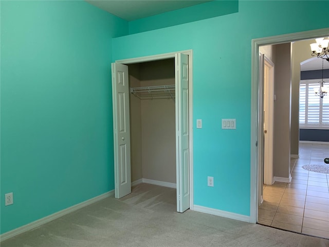 unfurnished bedroom featuring light colored carpet, a notable chandelier, and a closet