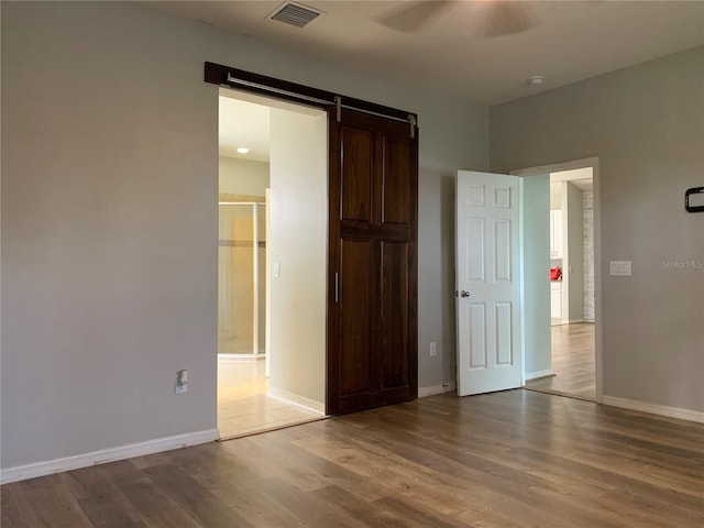 unfurnished bedroom featuring a barn door, wood-type flooring, and ceiling fan