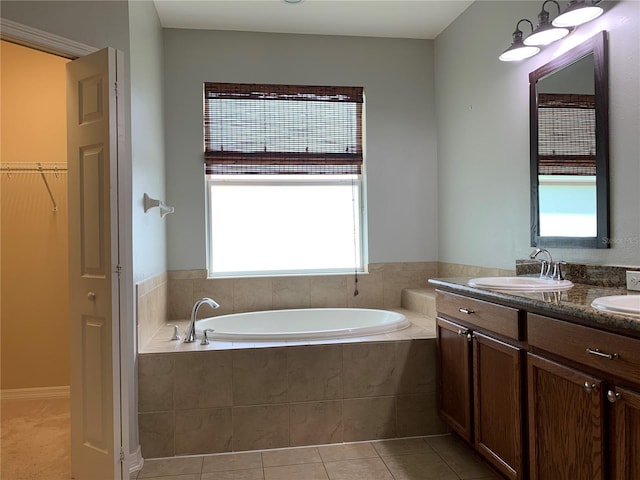 bathroom with tile patterned flooring, a relaxing tiled tub, and vanity