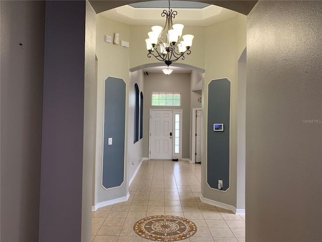 entryway featuring a raised ceiling, a chandelier, a high ceiling, and light tile patterned flooring