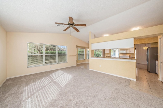 unfurnished living room with light carpet, a textured ceiling, ceiling fan with notable chandelier, and lofted ceiling