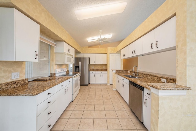 kitchen featuring white cabinetry, sink, stainless steel appliances, dark stone counters, and vaulted ceiling