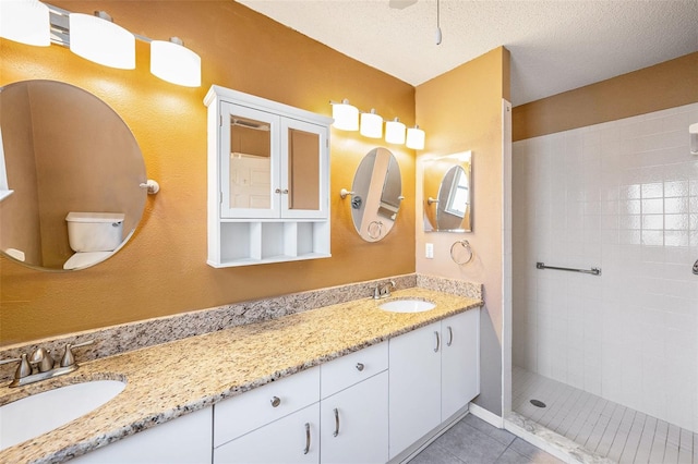 bathroom featuring a tile shower, tile patterned flooring, a textured ceiling, toilet, and vanity