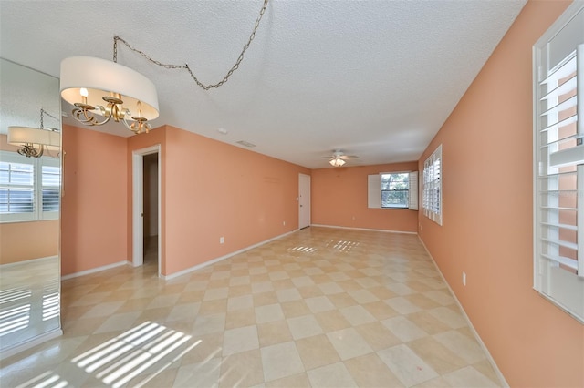 empty room with ceiling fan with notable chandelier and a textured ceiling