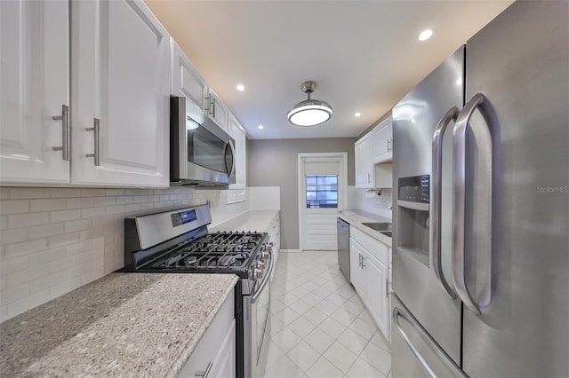 kitchen featuring appliances with stainless steel finishes, light stone counters, backsplash, light tile patterned floors, and white cabinetry