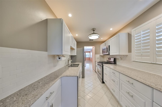 kitchen with light tile patterned flooring, appliances with stainless steel finishes, tasteful backsplash, white cabinets, and light stone countertops