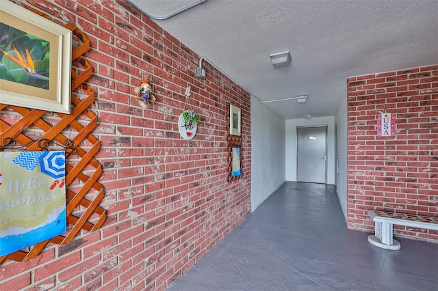 hallway featuring brick wall and a textured ceiling