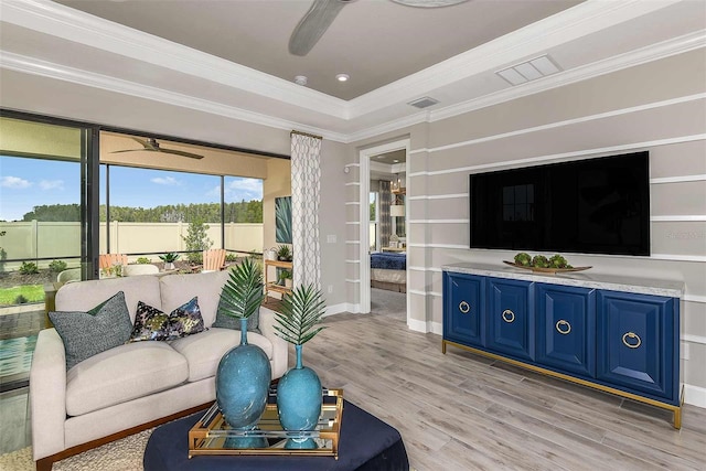 living room featuring ceiling fan, a tray ceiling, ornamental molding, and light wood-type flooring