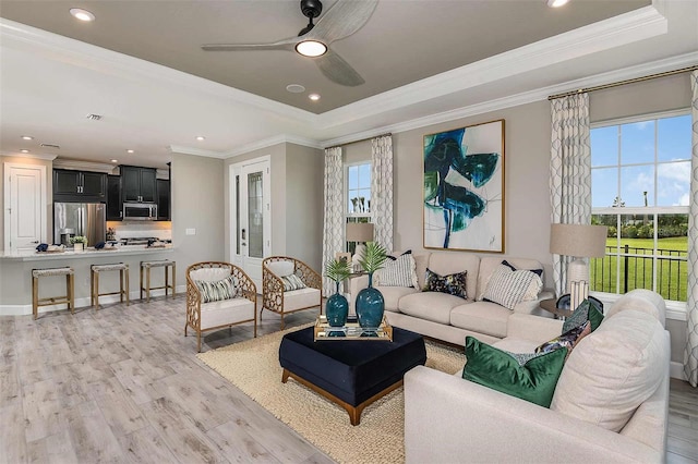 living room with ceiling fan, a tray ceiling, light hardwood / wood-style flooring, and crown molding