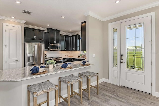 kitchen featuring appliances with stainless steel finishes, light hardwood / wood-style floors, kitchen peninsula, light stone counters, and a breakfast bar area