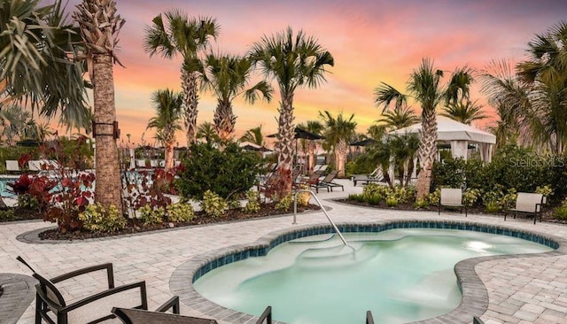 pool at dusk with a hot tub and a patio