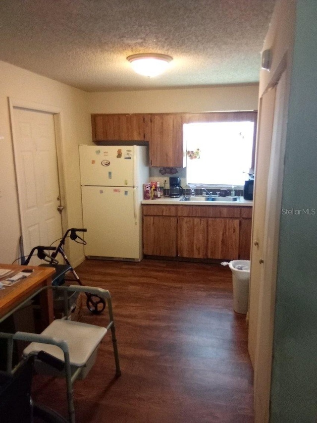 kitchen with brown cabinets, dark wood-type flooring, freestanding refrigerator, light countertops, and a sink