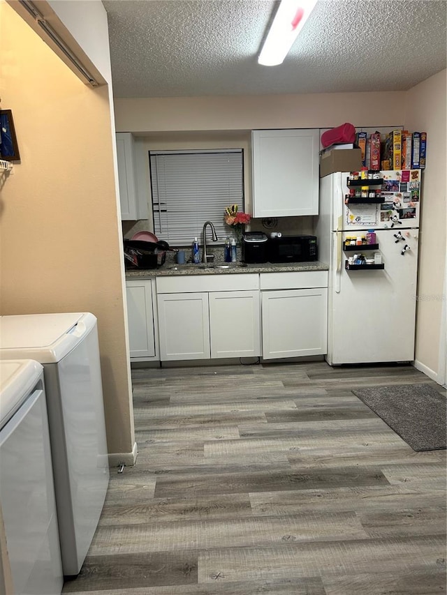 clothes washing area with light wood finished floors, a textured ceiling, washer and clothes dryer, and a sink