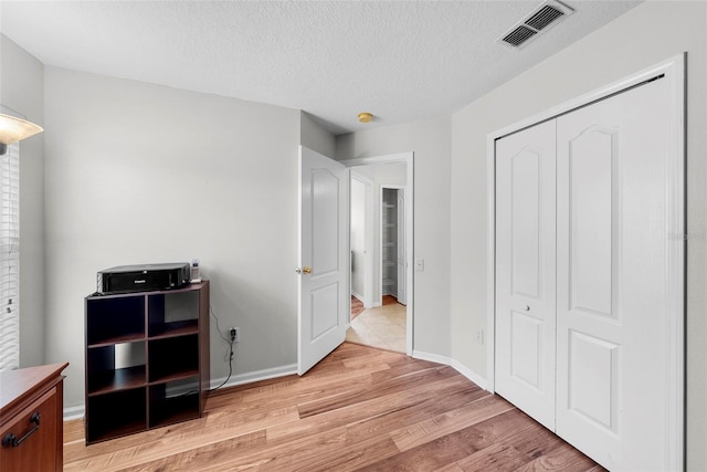 bedroom with a closet, light hardwood / wood-style floors, and a textured ceiling