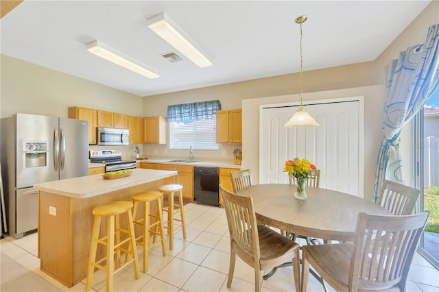 kitchen featuring pendant lighting, a center island, light brown cabinets, stainless steel appliances, and light tile patterned flooring