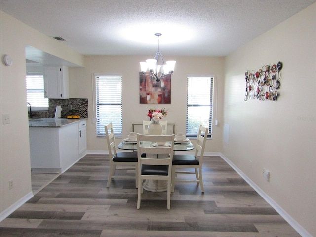 dining space with a textured ceiling, dark hardwood / wood-style flooring, a healthy amount of sunlight, and a notable chandelier