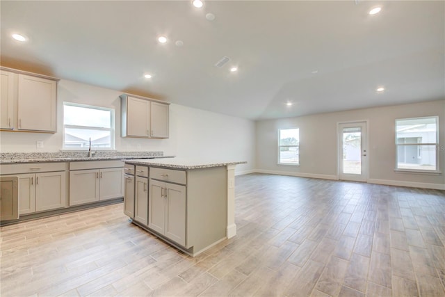 kitchen with sink, gray cabinets, a center island, light hardwood / wood-style floors, and light stone countertops