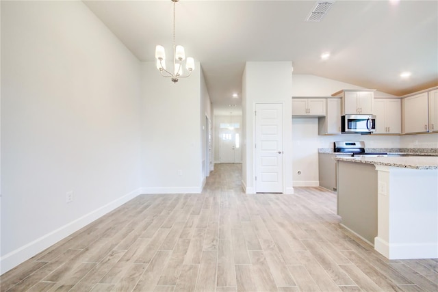 kitchen with lofted ceiling, decorative light fixtures, appliances with stainless steel finishes, light stone countertops, and light hardwood / wood-style floors