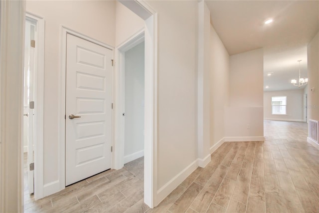 hallway with a notable chandelier and light wood-type flooring