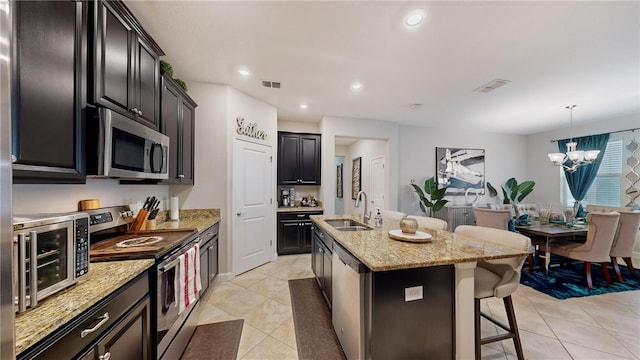 kitchen with appliances with stainless steel finishes, an island with sink, pendant lighting, sink, and a notable chandelier