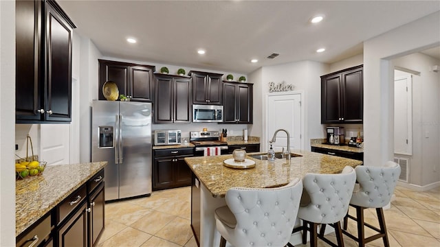 kitchen featuring light stone counters, a center island with sink, appliances with stainless steel finishes, and sink