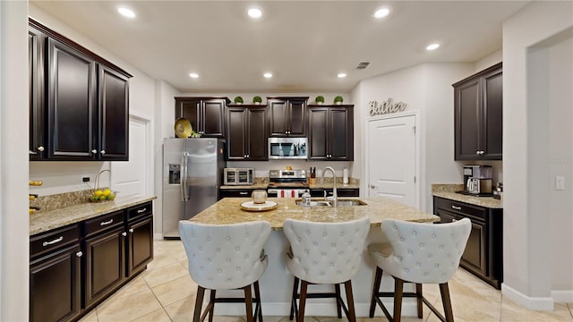 kitchen with light tile patterned flooring, sink, dark brown cabinets, a kitchen island with sink, and appliances with stainless steel finishes