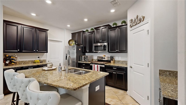 kitchen featuring an island with sink, sink, stainless steel appliances, a breakfast bar area, and light stone countertops