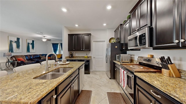 kitchen with stainless steel appliances, light stone counters, a center island with sink, and sink