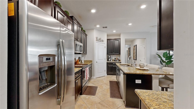 kitchen featuring light tile patterned flooring, a kitchen island with sink, sink, stainless steel appliances, and light stone countertops