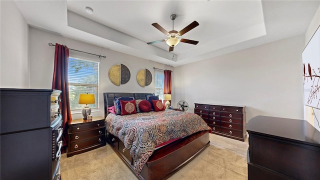 carpeted bedroom with ceiling fan and a tray ceiling