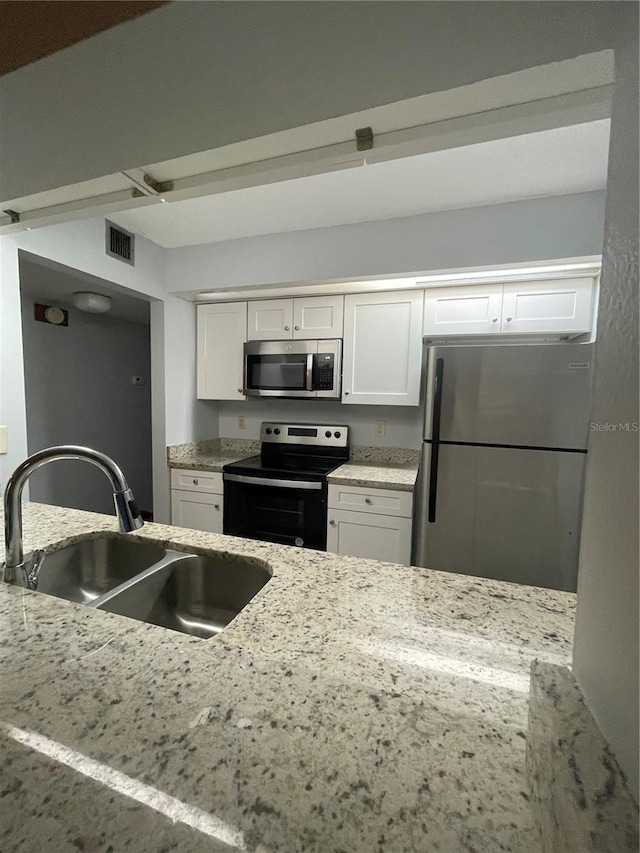 kitchen featuring white cabinetry, stainless steel appliances, light stone countertops, and sink