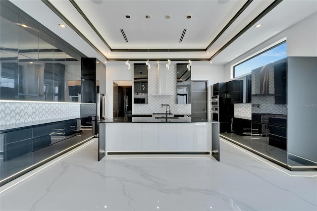 kitchen with dark stone countertops, backsplash, a tray ceiling, and sink