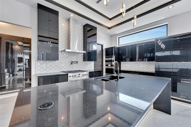 kitchen featuring appliances with stainless steel finishes, wall chimney range hood, dark stone counters, an island with sink, and decorative backsplash