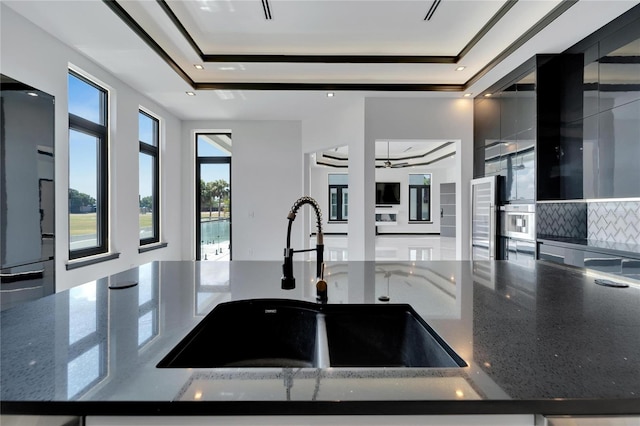 kitchen with a raised ceiling, decorative backsplash, dark stone counters, and sink