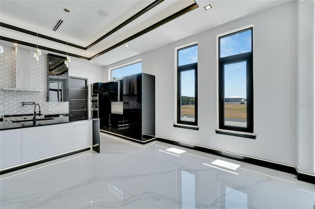 kitchen featuring sink, backsplash, white cabinets, and decorative light fixtures