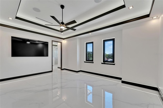 interior space with ceiling fan, tile walls, a tray ceiling, and crown molding