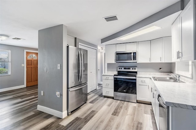 kitchen with white cabinets, light hardwood / wood-style floors, appliances with stainless steel finishes, and sink