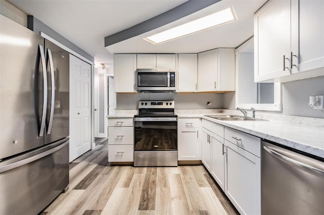 kitchen with appliances with stainless steel finishes, light wood-type flooring, light stone counters, and white cabinets