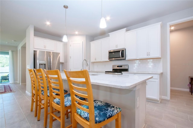 kitchen with decorative light fixtures, a kitchen island with sink, stainless steel appliances, and white cabinetry